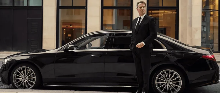 a professional limousine chauffeur in front of the passenger door of a mercedes Orionis Chauffeur services